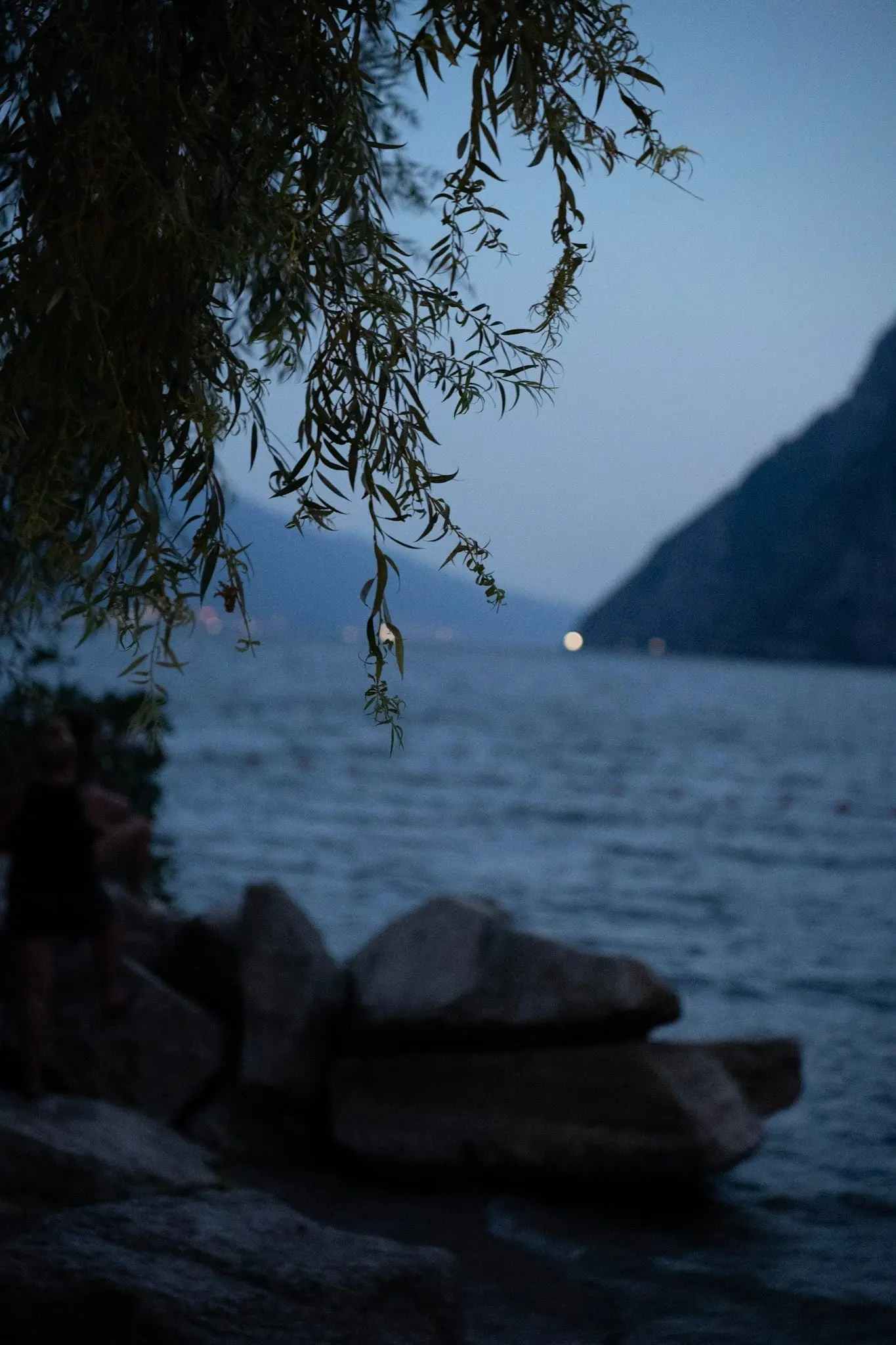 Bergsee in der Abenddämmerung mit Felsen im Vordergrund