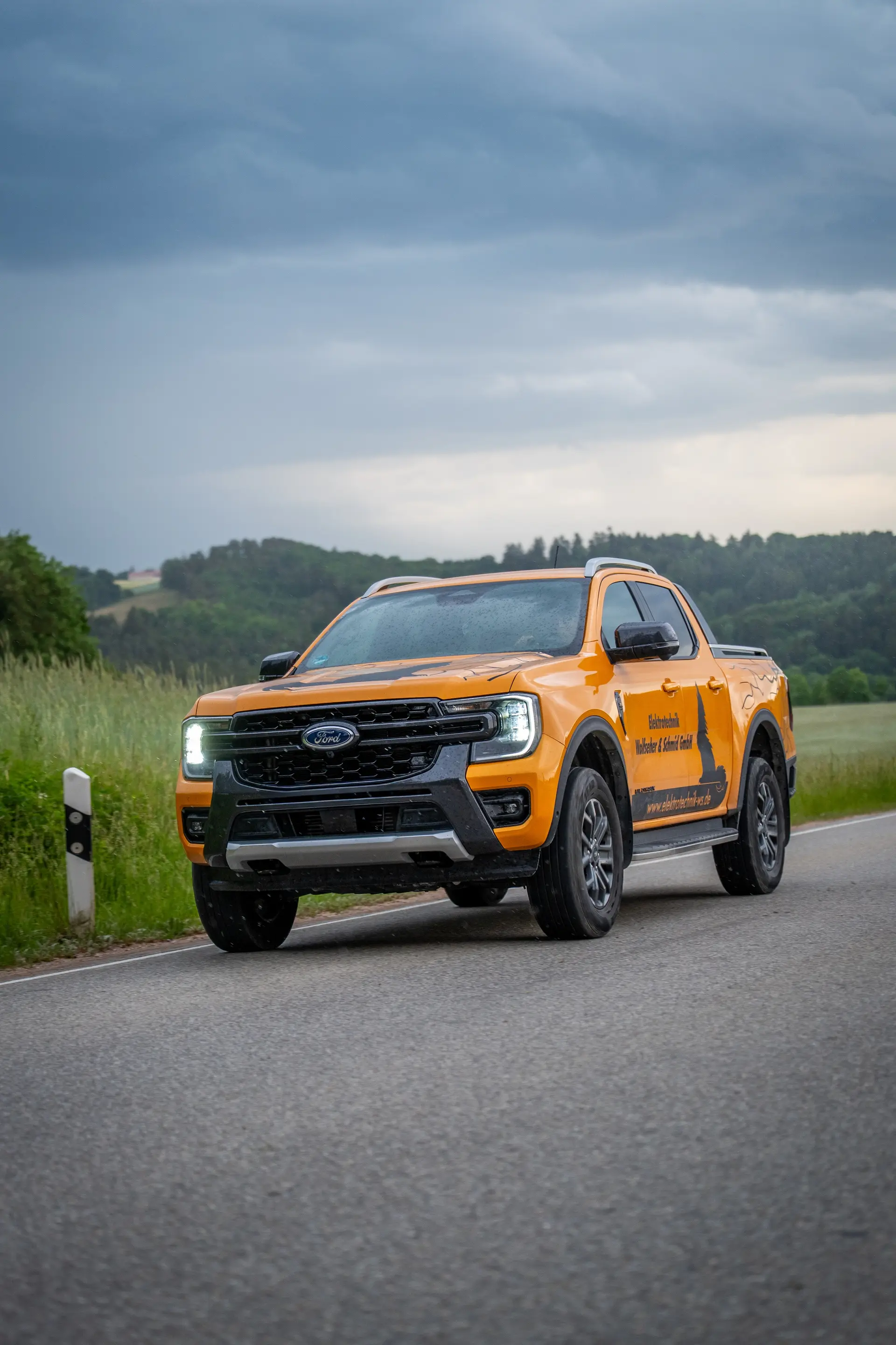 Orangefarbener Pick-up auf einer Landstraße vor bewölktem Himmel