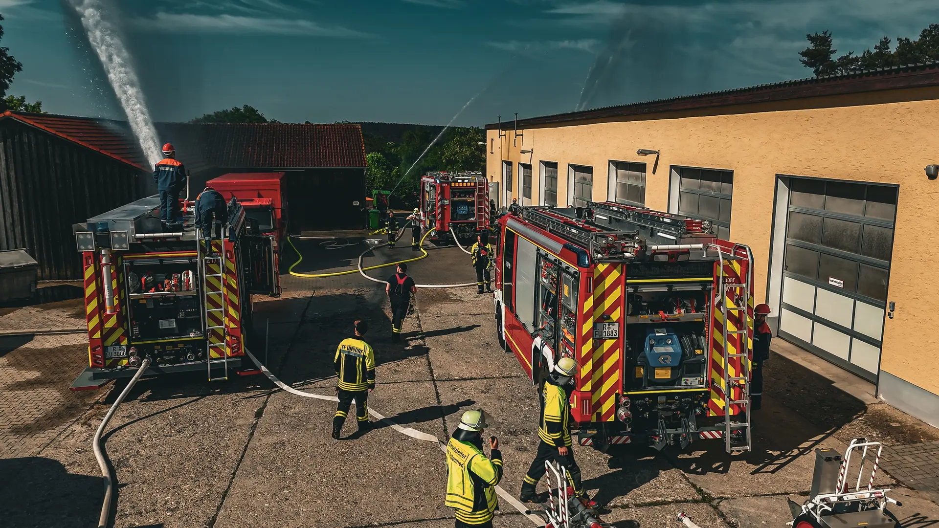 Feuerwehrübung vor dem Gerätehaus mit zwei Löschfahrzeugen und Wasserstrahl