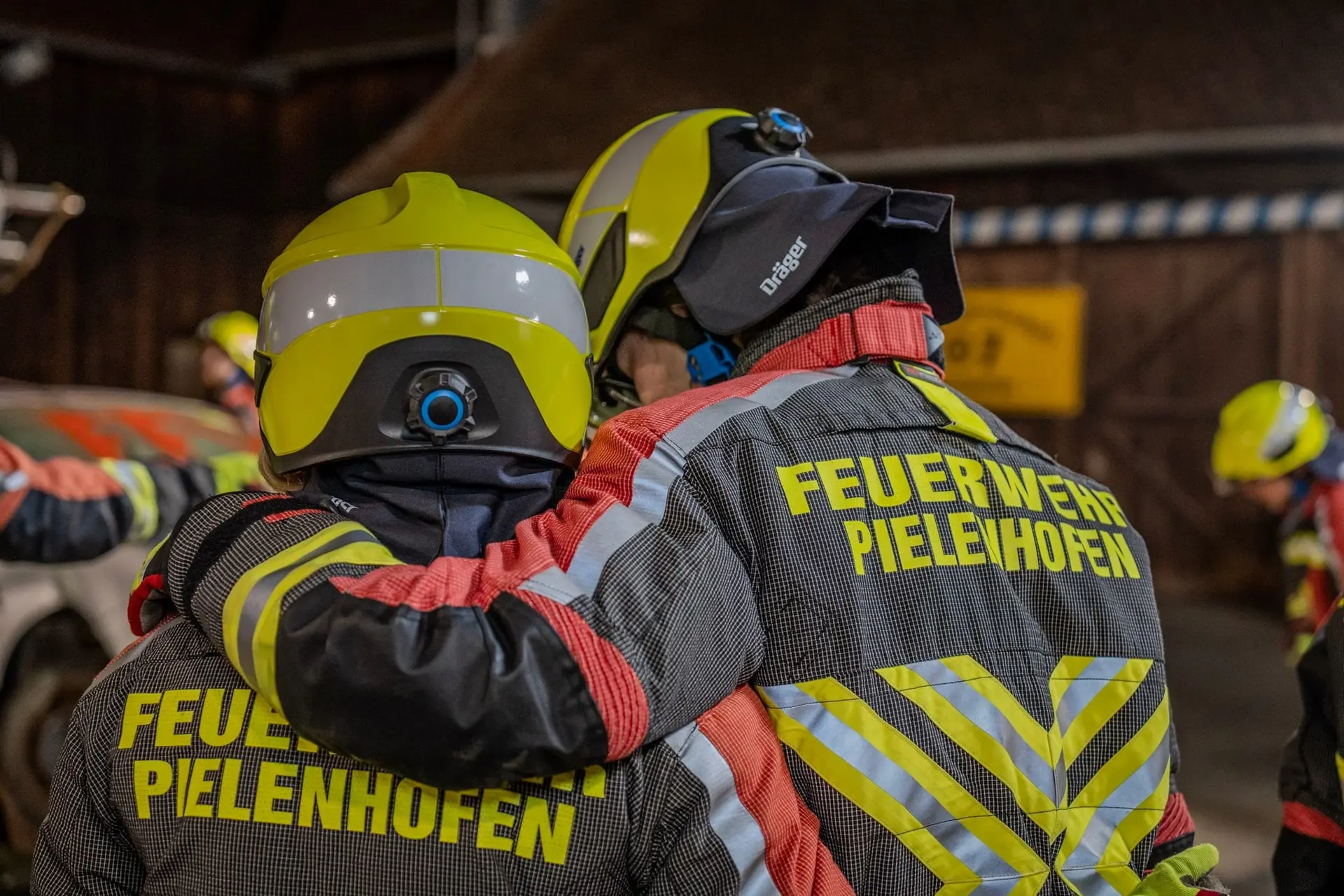 Zwei Feuerwehrleute Arm in Arm, von hinten fotografiert