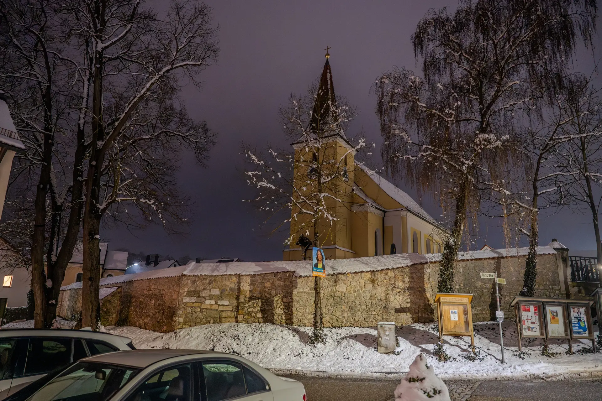 Verschneite Kirche mit Friedhofsmauer bei Nacht