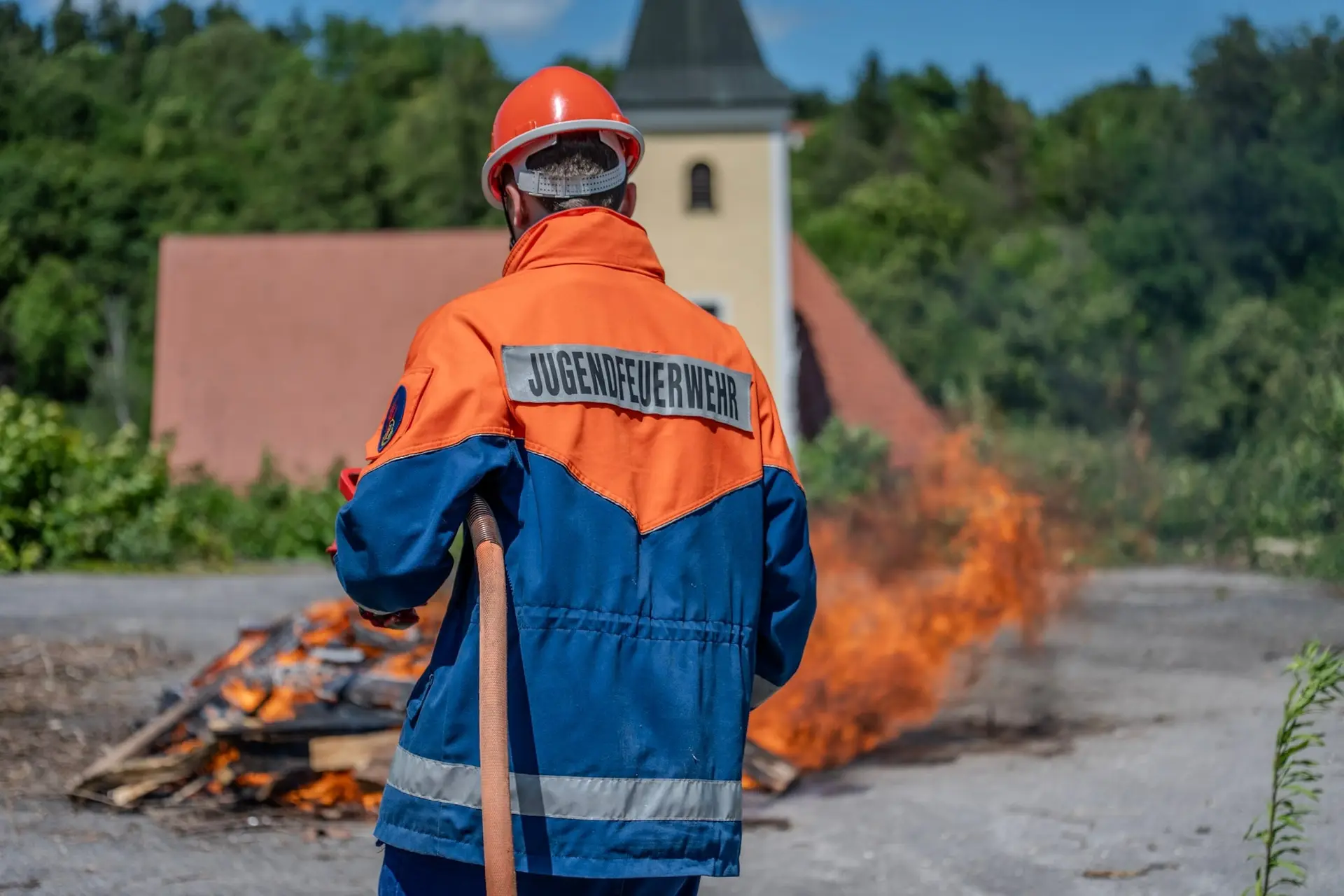 Mitglied der Jugendfeuerwehr vor einem Übungsfeuer, von hinten fotografiert