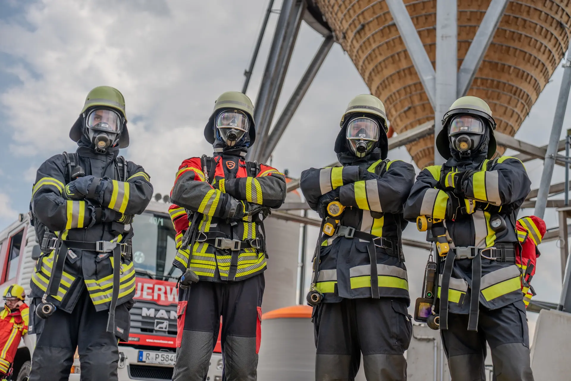 Vier Atemschutzträger der Feuerwehr stehen vor einem Übungsturm