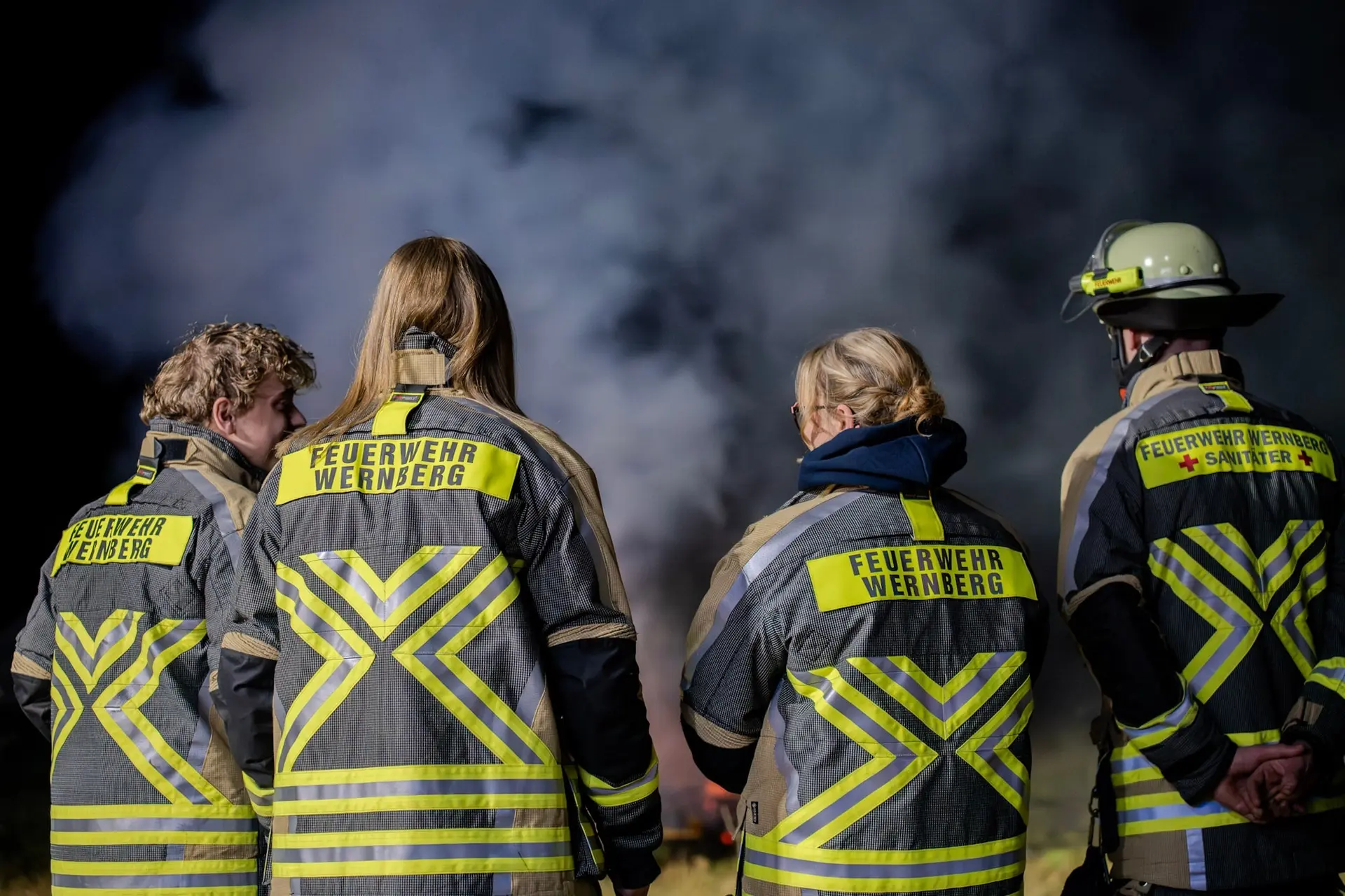 Feuerwehrleute mit Rückenaufdruck „Feuerwehr Wernberg“ vor Rauchschwaden, von hinten fotografiert