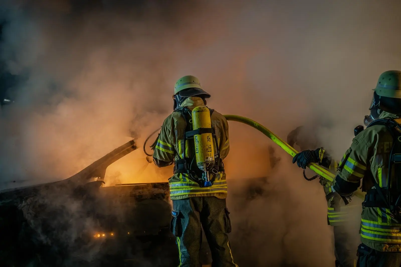 Einsatzkräfte der Feuerwehr löschen nachts einen brennenden Pkw