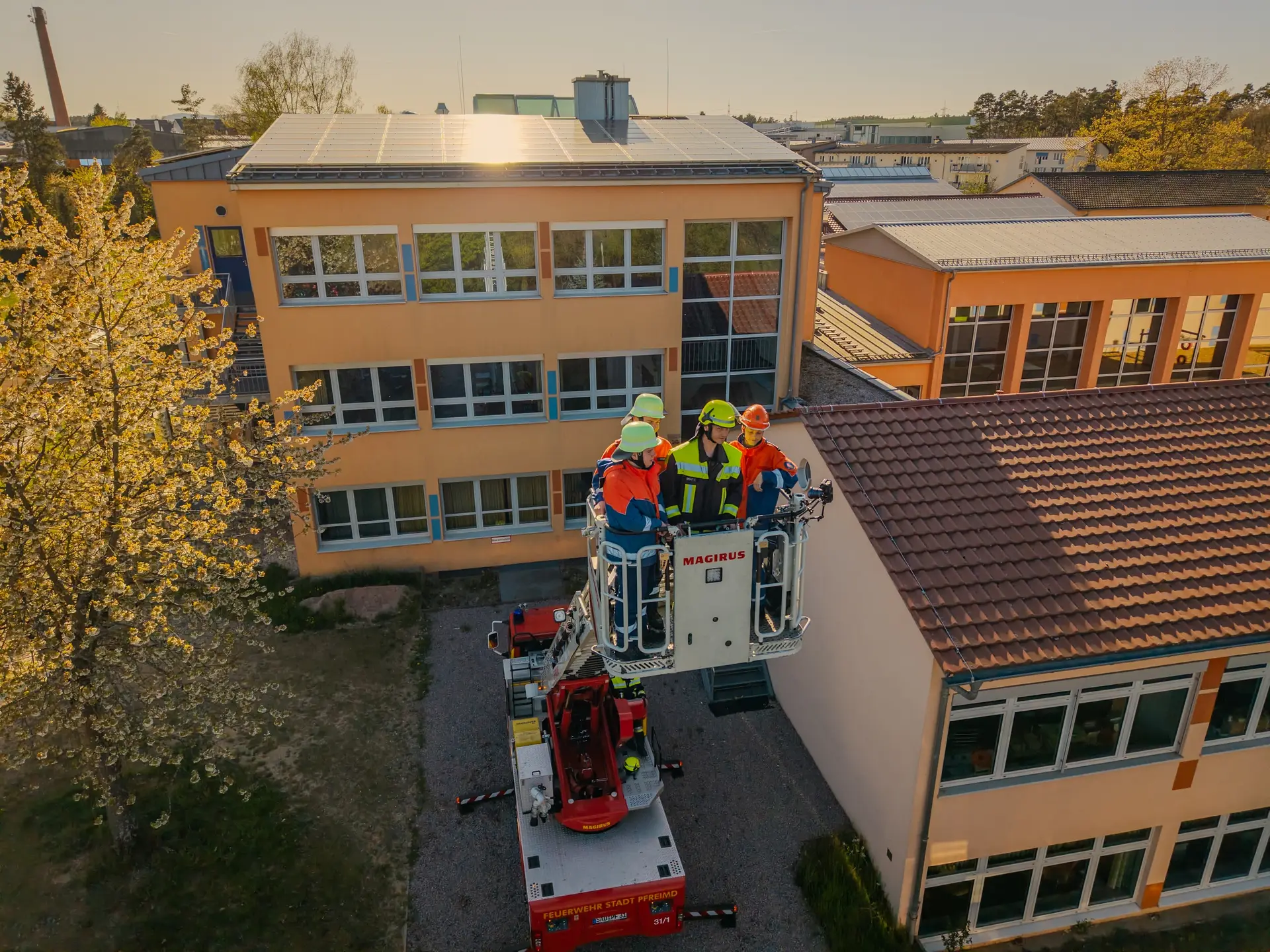 Drehleiterkorb mit Einsatzkräften vor einem Schulgebäude, aus der Luft fotografiert