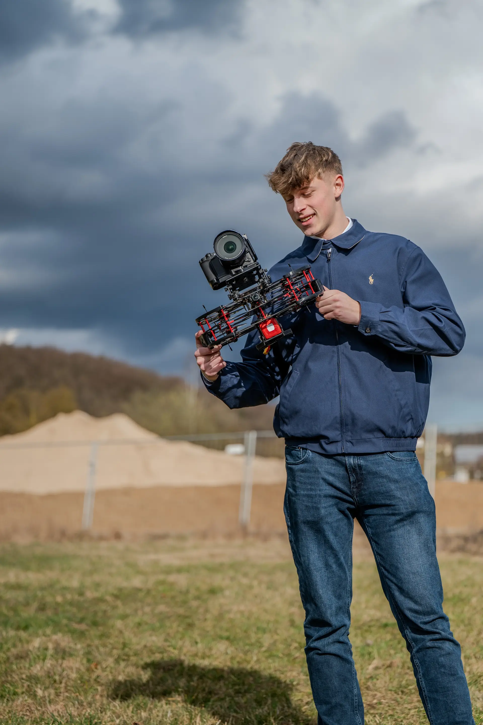 Kameramann hält eine FPV-Kameradrohne auf einer Wiese unter Wolkenhimmel