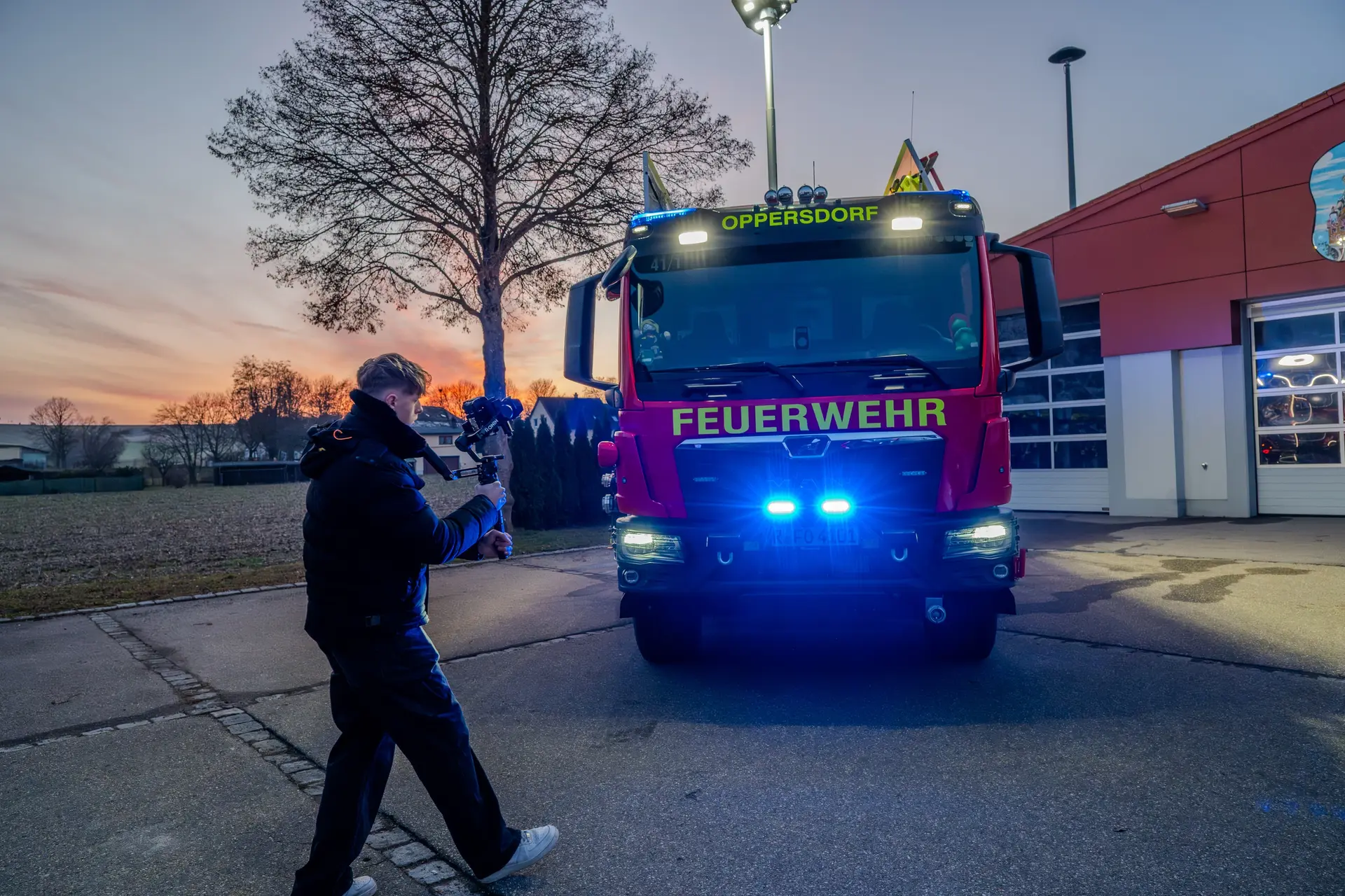 Kameramann filmt mit Gimbal ein Löschfahrzeug mit Blaulicht vor dem Gerätehaus in der Abenddämmerung