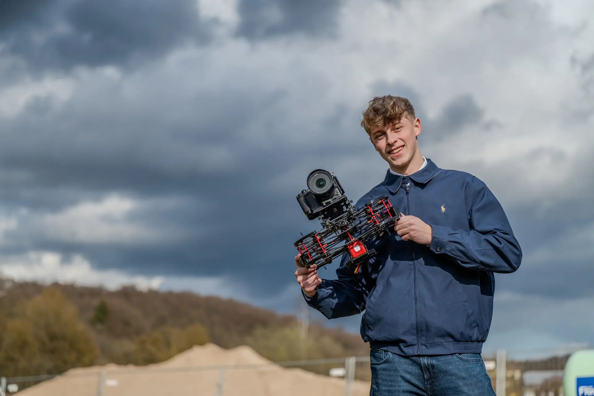 Kameramann hält lächelnd eine FPV-Kameradrohne vor bewölktem Himmel
