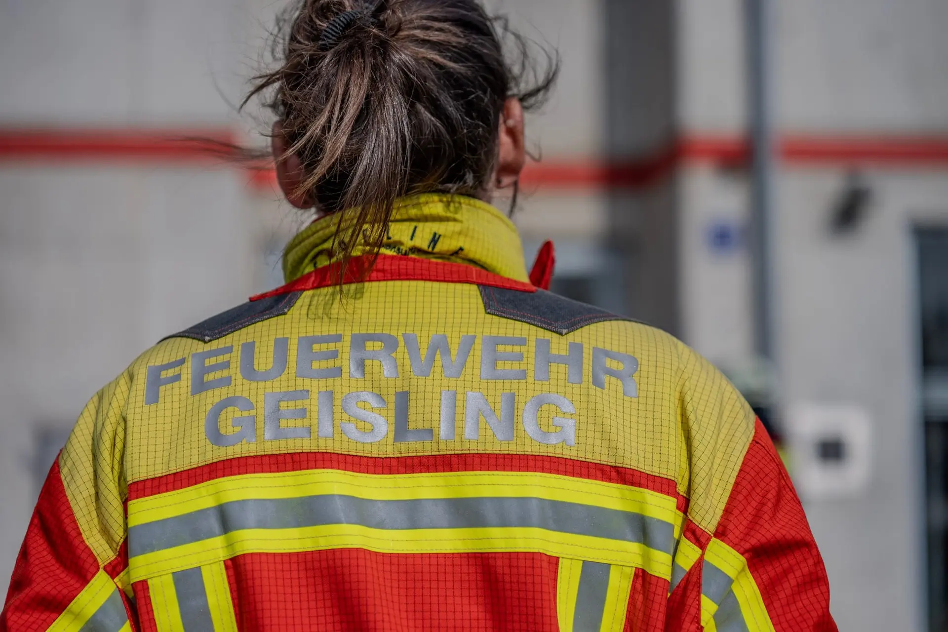 Feuerwehrfrau in Einsatzjacke, von hinten fotografiert