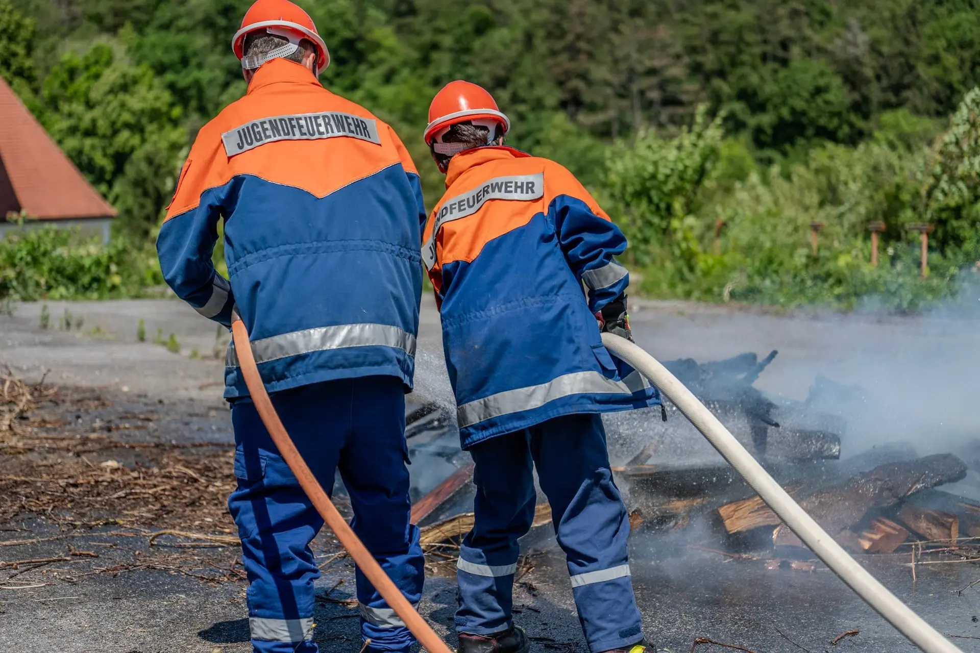 Zwei Mitglieder der Jugendfeuerwehr löschen ein Feuer, von hinten fotografiert