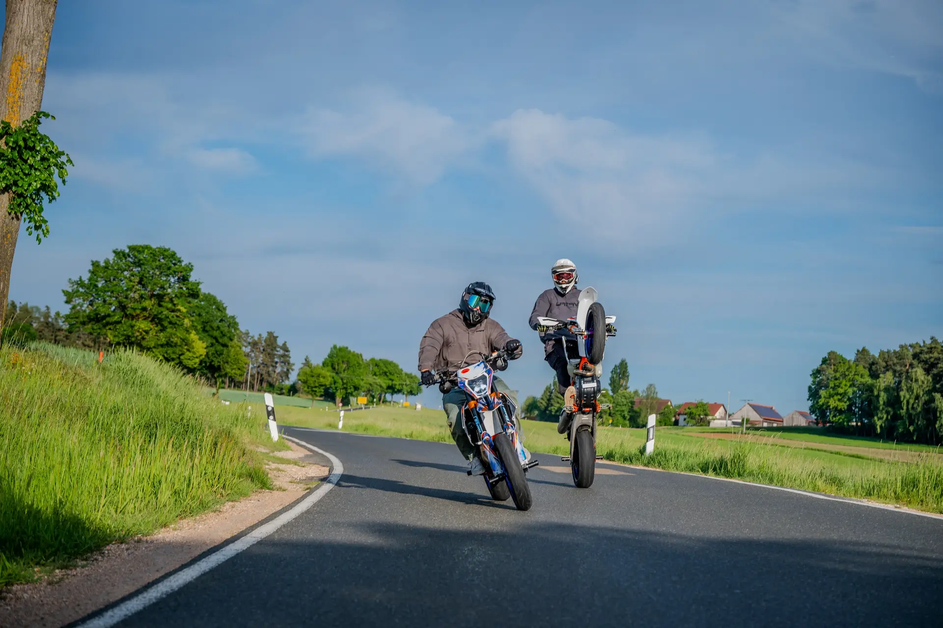 Zwei Motorradfahrer auf einer Landstraße, einer fährt auf dem Hinterrad