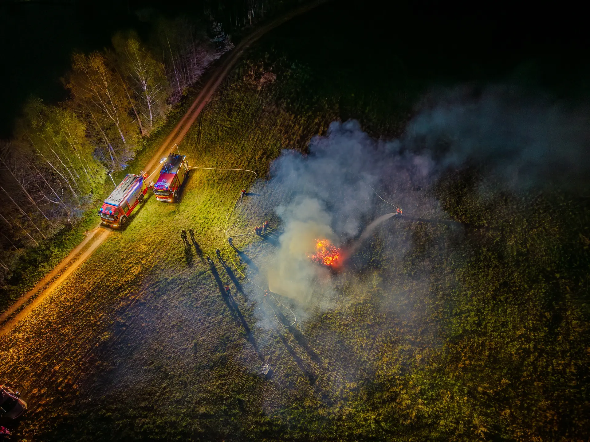 Nächtliche Übung aus der Luft: Feuerwehrfahrzeuge und Rauch über einer Wiese