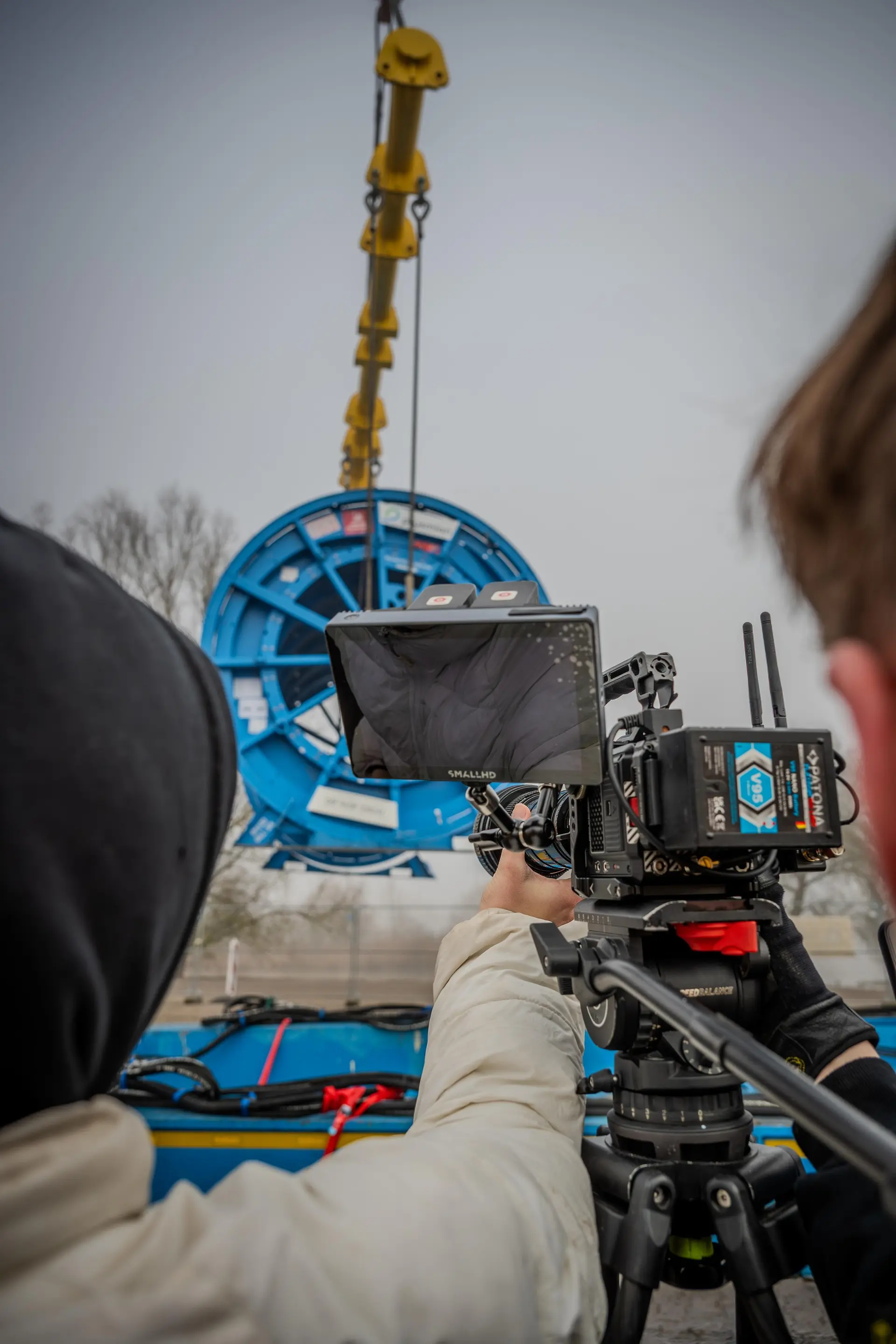 Kamera mit Monitor auf einem Stativ filmt das Anheben einer großen Kabeltrommel