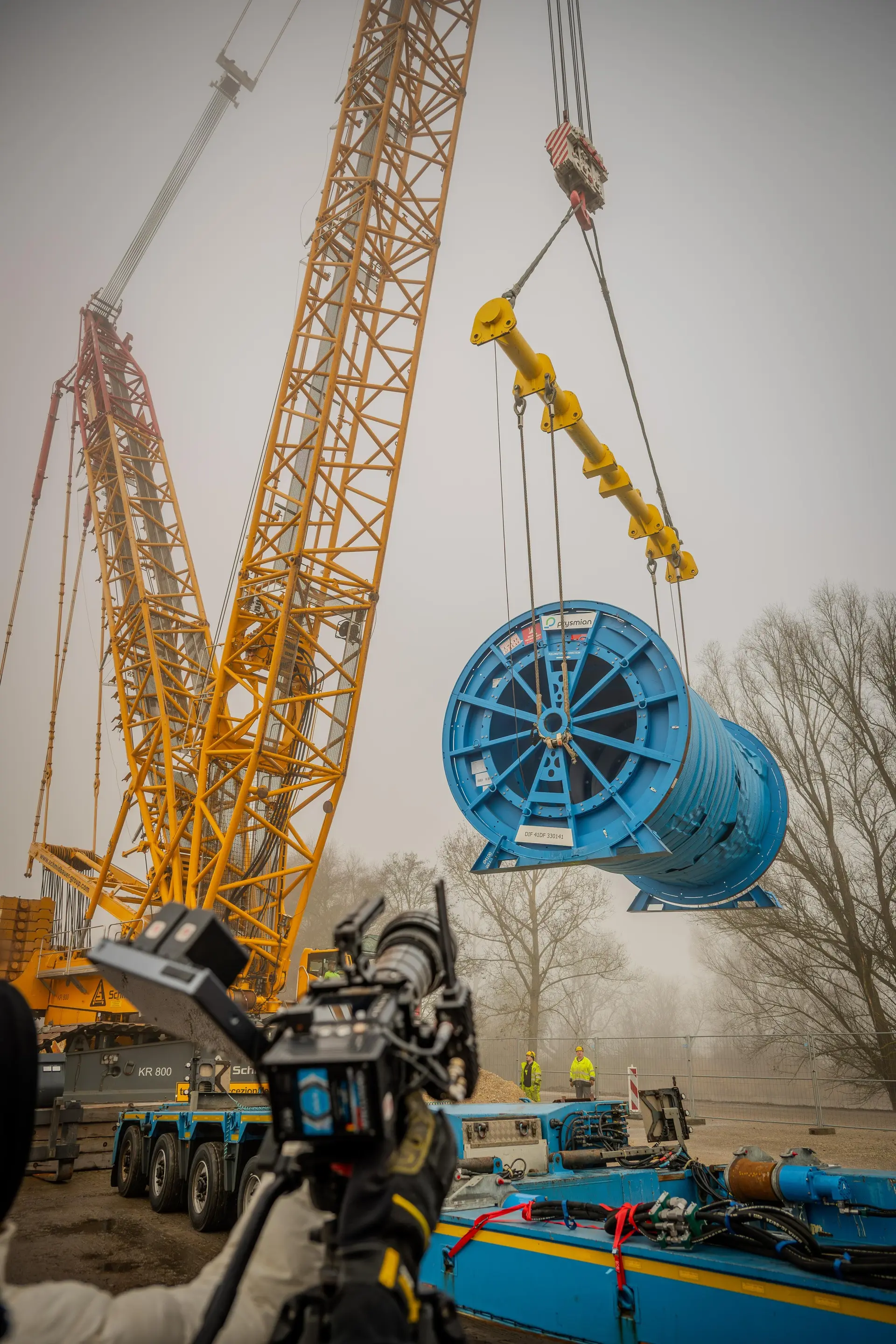 Dreh auf einer Baustelle: Kamera filmt, wie ein Raupenkran eine große Kabeltrommel anhebt